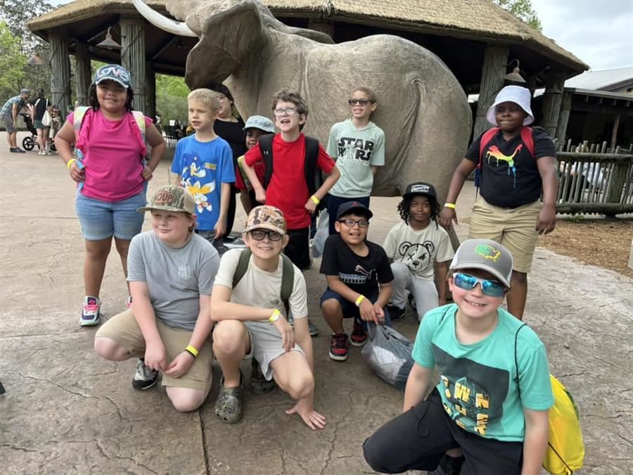 Twelve students posing in front of a concrete statue of an elephant at the zoo.